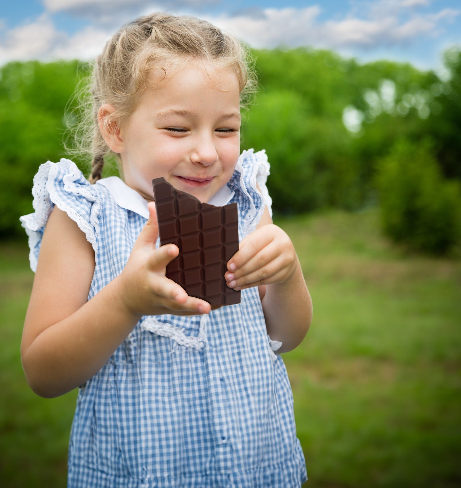 Little girl enjoying and laughing while eating a piece of Belgian Rice Milk Chocolate from FOODIES-PLANET.